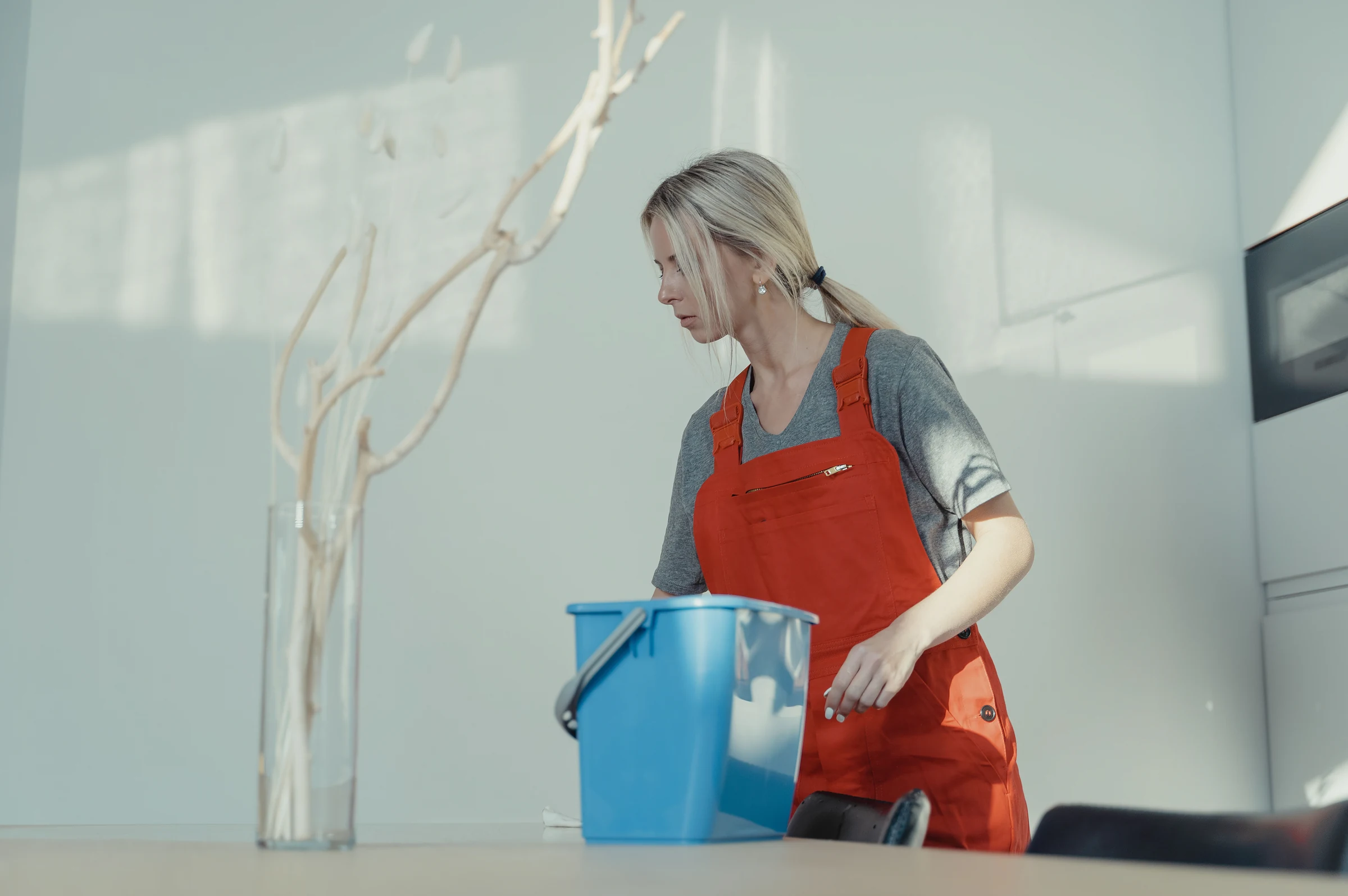 A cleaner in overalls preparing a bucket in a kitchen