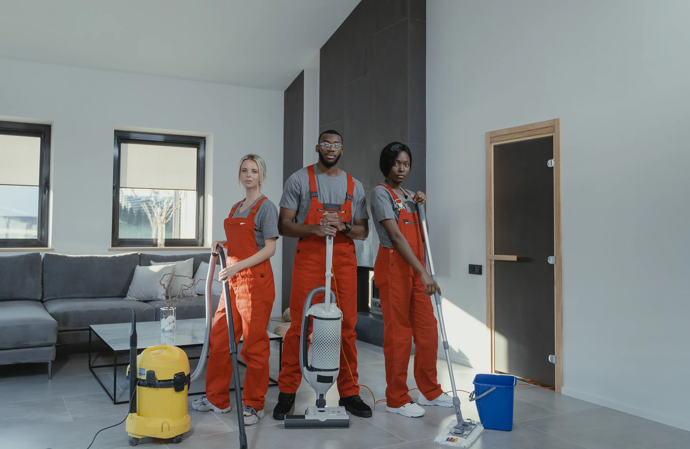A three-person cleaning crew with vacuums and mops in a living room