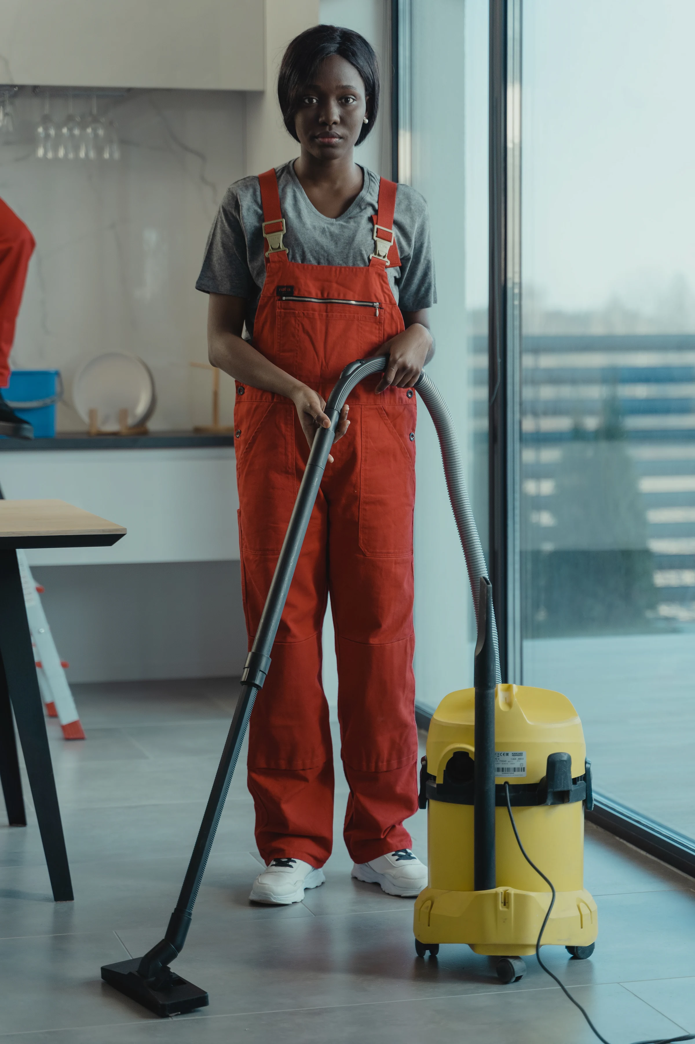 A cleaner in work overalls vacuuming a bright living room
