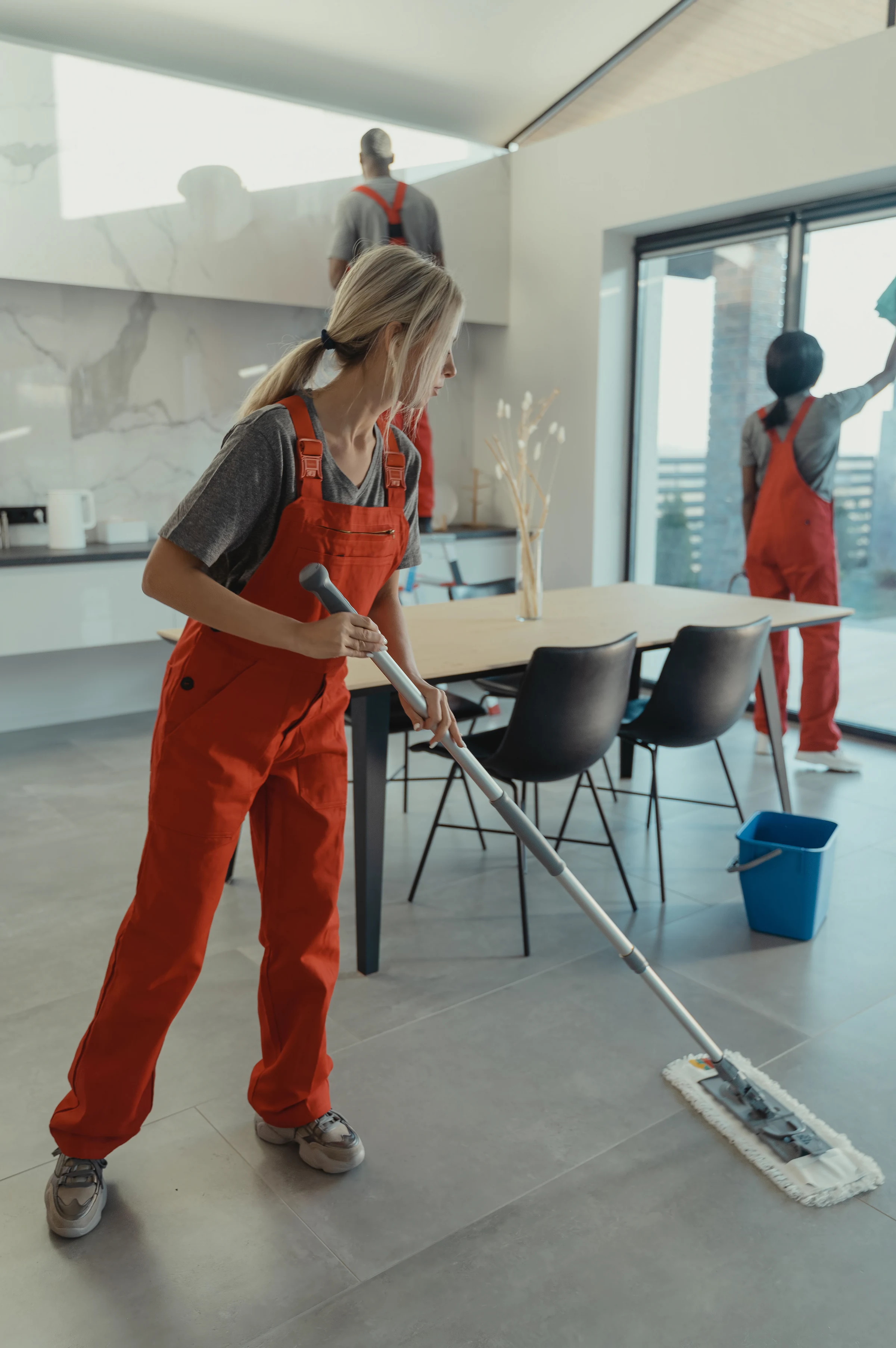 A cleaner mopping a kitchen floor while colleagues clean the windows