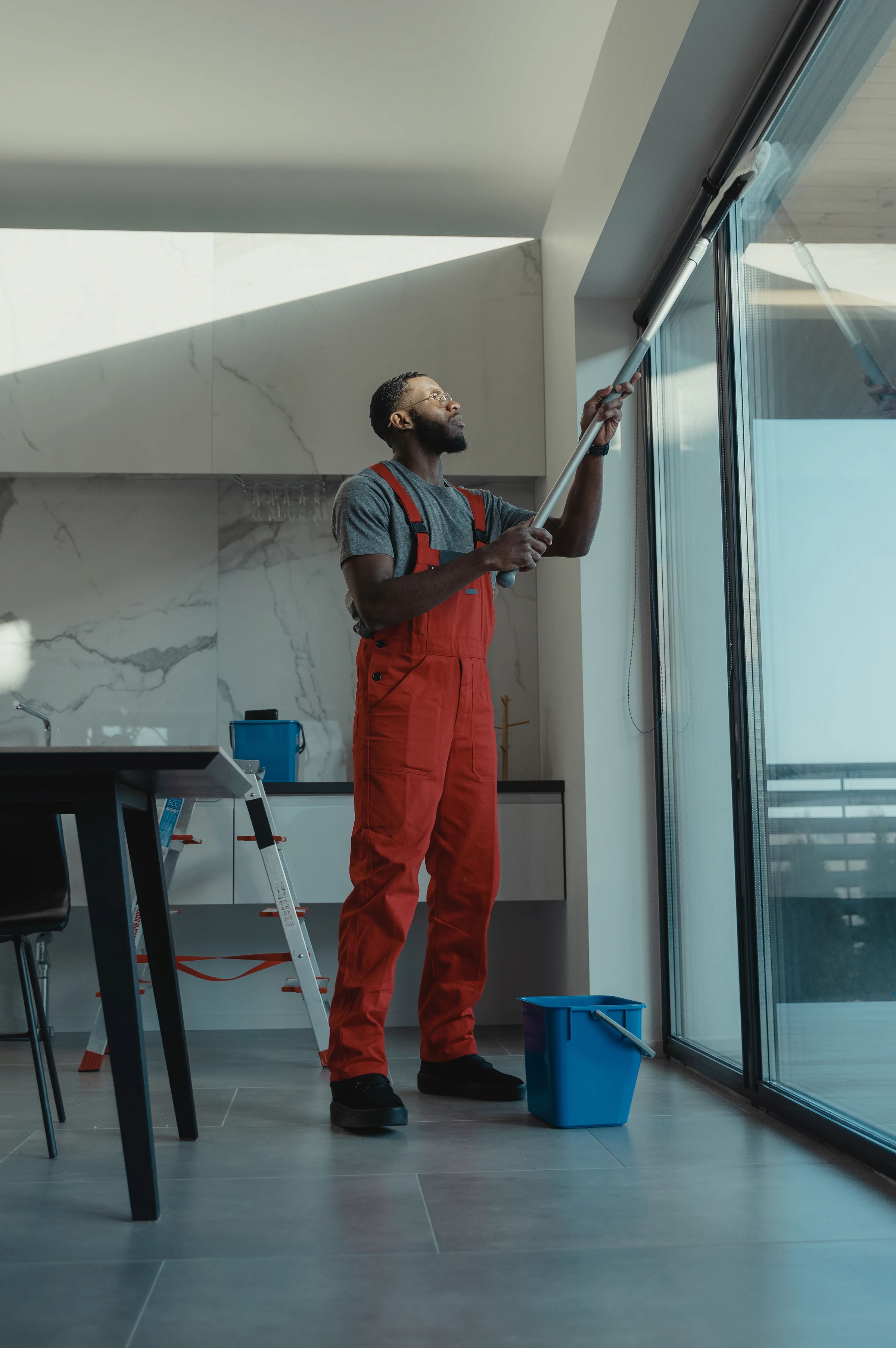 A cleaner dusting the top of a tall window frame